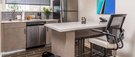 A modern kitchen with a built-in dishwasher, stainless steel appliances, and a dining area with a chair and table.
