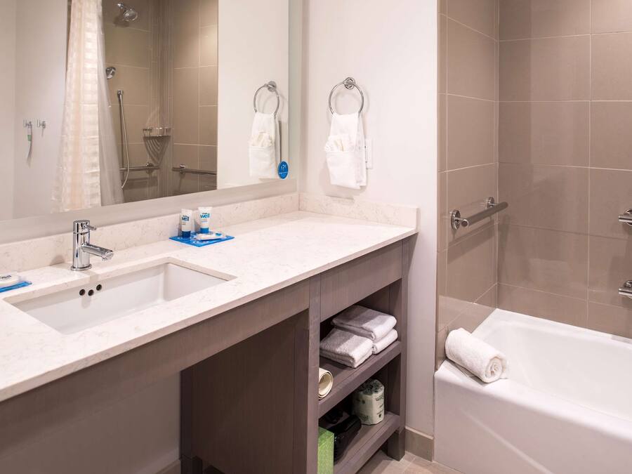 Un baño con lavamanos, espejo y bañera. Hay toallas y artículos de aseo en la encimera.