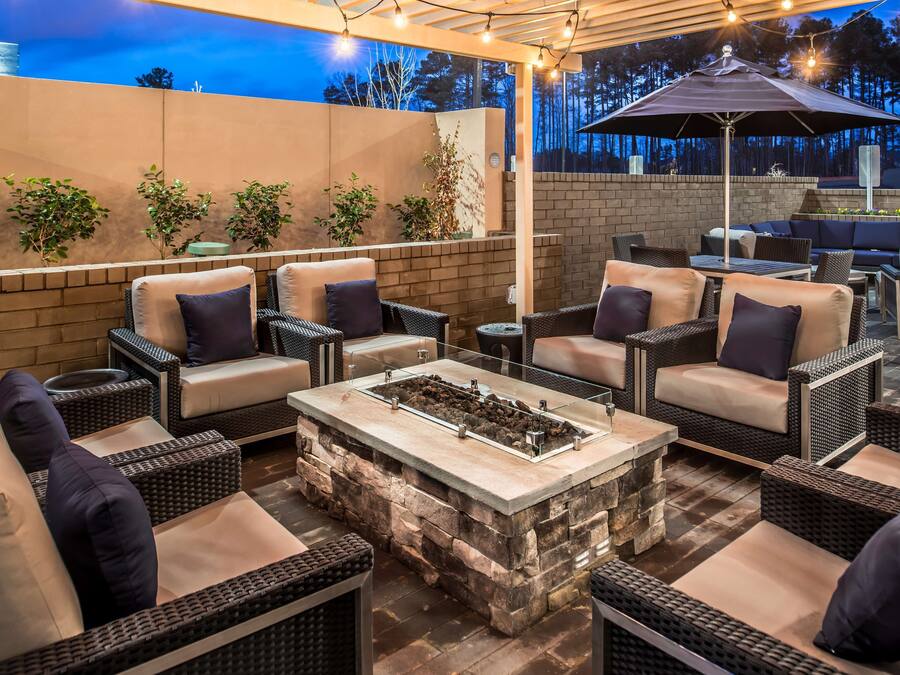 An outdoor patio area with wicker furniture, a stone fire table, and string lights.