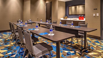 A conference room with a long table, chairs, water bottles, and a kitchen area in the background.