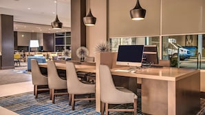 A modern hotel lobby with a reception desk, several chairs, a large monitor, and pendant lighting. - Hyatt House Raleigh / RDU / Brier Creek (Raleigh)