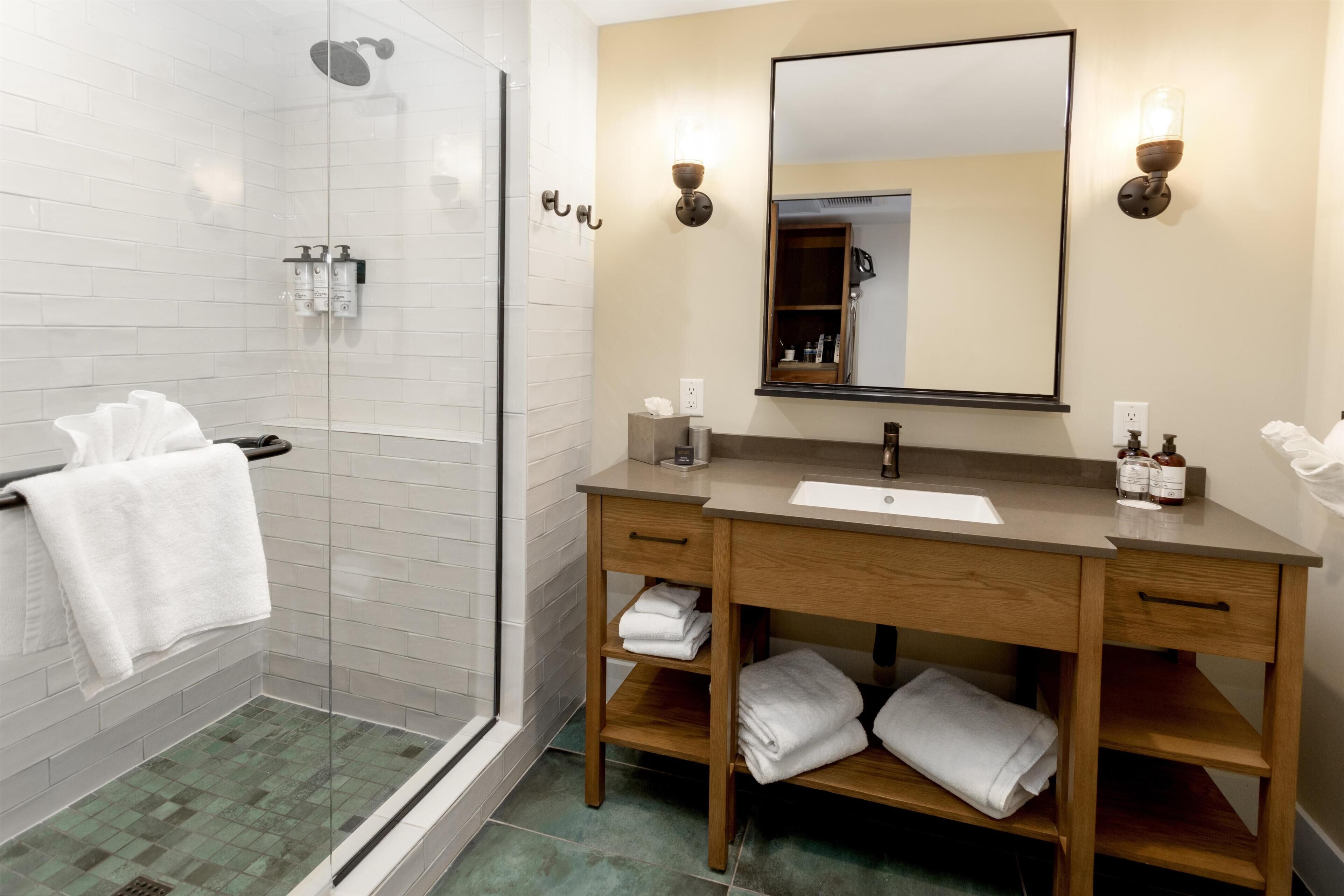 A modern bathroom with a glass shower, wooden vanity, and a large mirror.