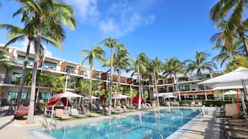 A hotel pool area with palm trees, lounge chairs, and umbrellas.