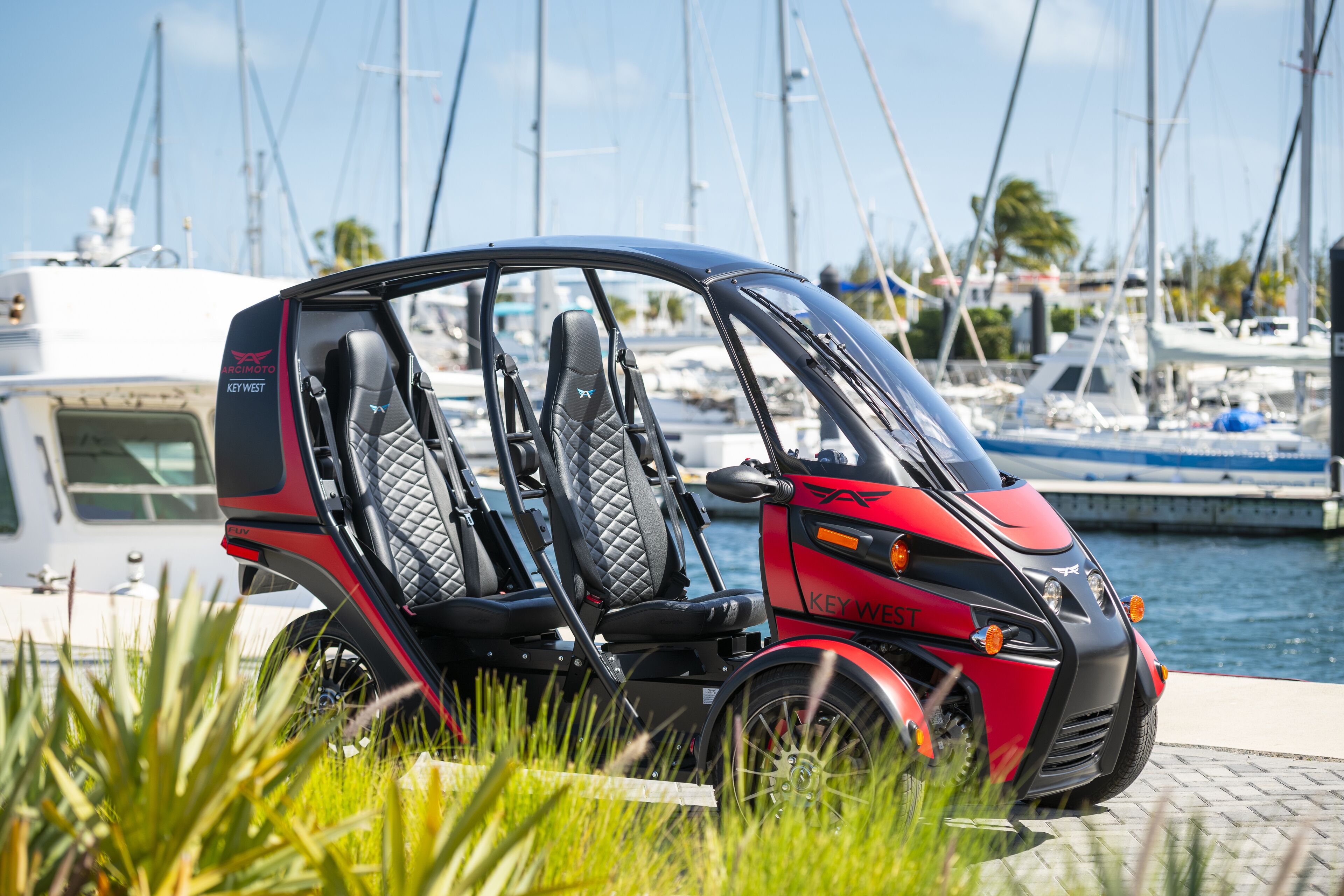 A red and black vehicle with "KEY WEST" written on it, parked near a marina with boats in the background.