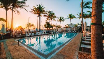 A swimming pool with lounge chairs and palm trees, surrounded by a paved area.
