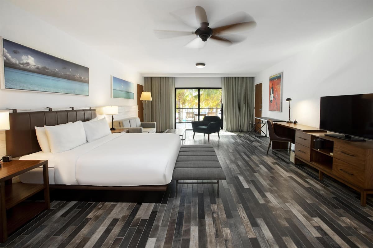 A hotel room with a large bed, a desk, a chair, a television, and a ceiling fan.