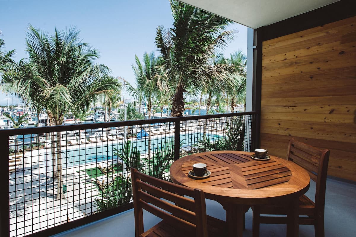 A balcony with a wooden table and chairs, overlooking a swimming pool and palm trees.
