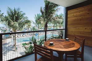 Un balcon avec une table et des chaises en bois, donnant sur une piscine et des palmiers.
