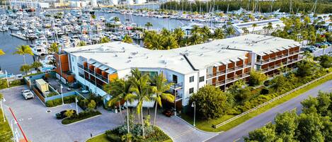 Un puerto deportivo con numerosos barcos, un edificio moderno de techo plano y un aparcamiento con jardín ajardinado.