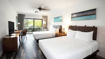 Habitación de hotel con dos camas, un escritorio con televisor y un balcón con vista al mar.