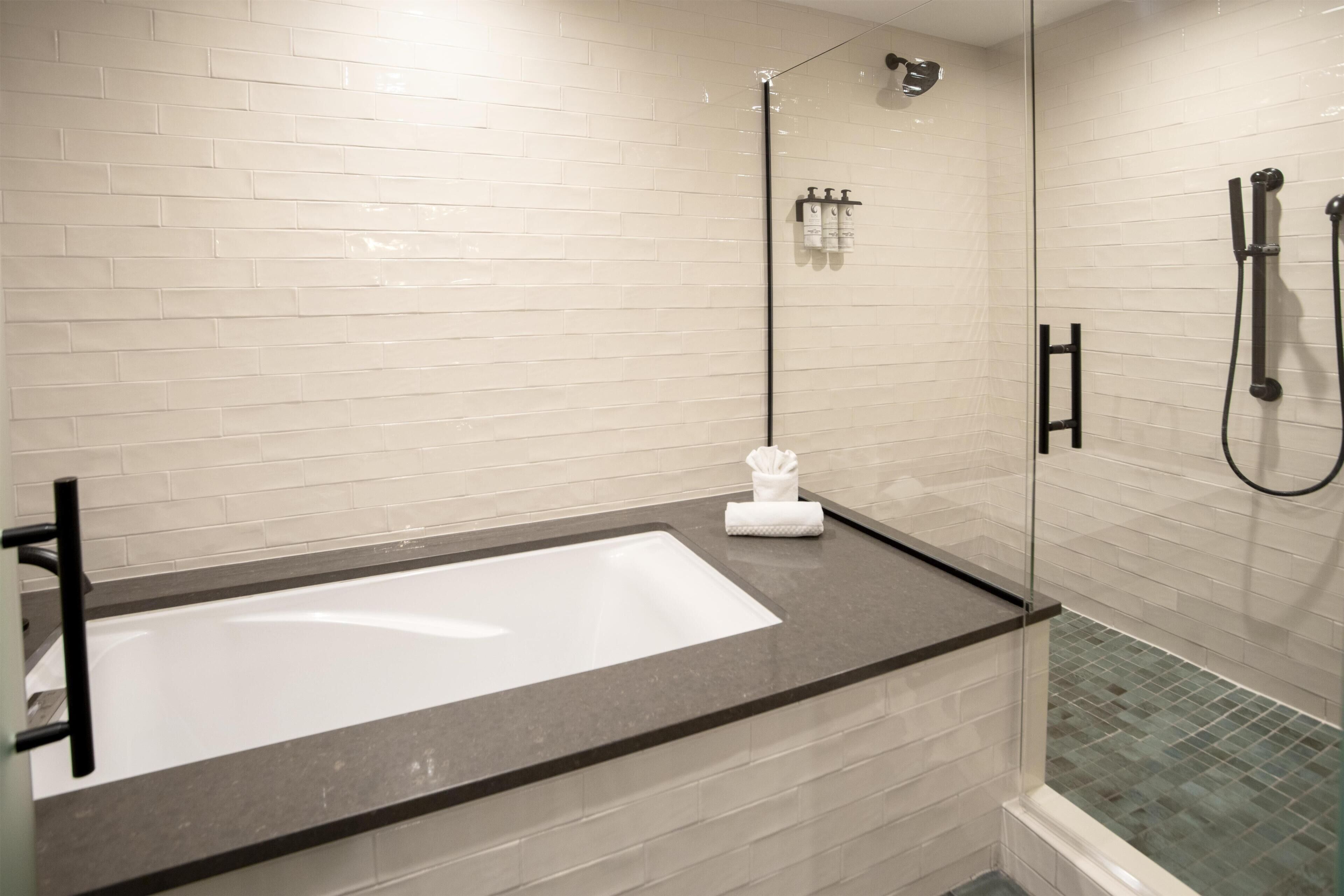 Un baño moderno con una bañera grande, una zona de ducha con mampara de vidrio y un revestimiento de azulejos.