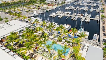 Un port de plaisance où sont amarrés de nombreux bateaux, une piscine entourée de palmiers et une vue sur les environs.
