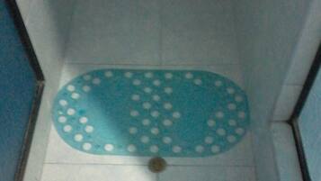 A bathroom with a blue floor mat featuring white dots, white tiled walls, and a visible drain in the center.