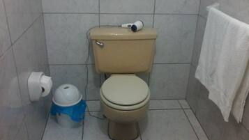 Un baño con un inodoro, un bote de basura azul y una toalla blanca colgada en la pared.