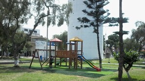 Un parque infantil con tobogán y estructuras para escalar, rodeado de césped y árboles.