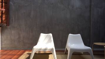 Two white plastic chairs on a beige rug against a grey wall with a wooden window frame.