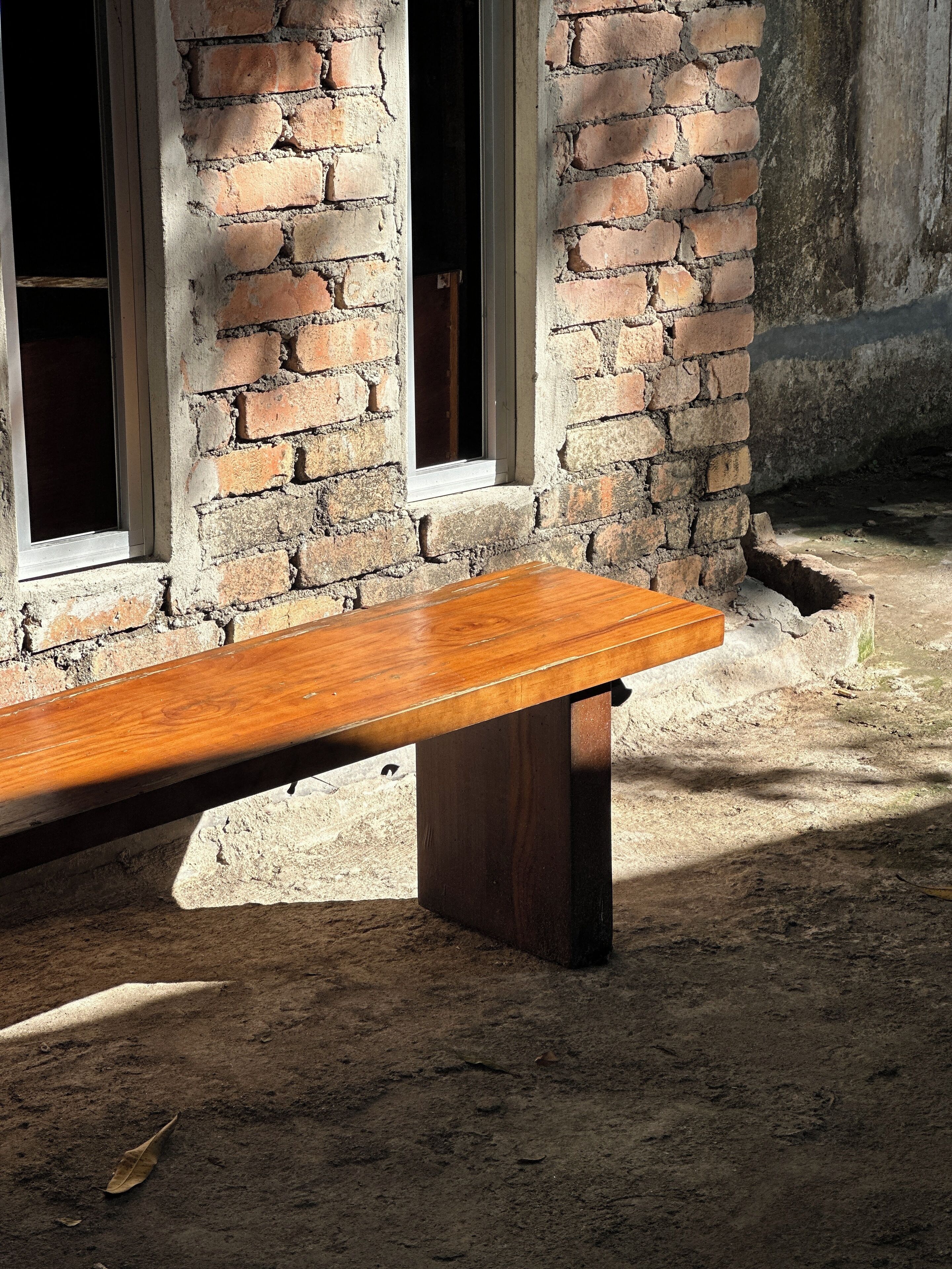 A wooden bench against a brick wall with windows.