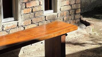 A wooden bench against a brick wall with windows.