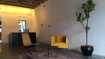 A modern interior with a wooden desk, a yellow armchair, a potted plant, and a red patterned rug.