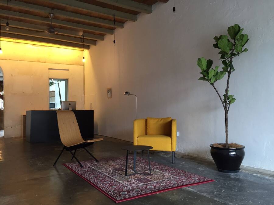 A modern interior with a wooden desk, a yellow armchair, a potted plant, and a red patterned rug.