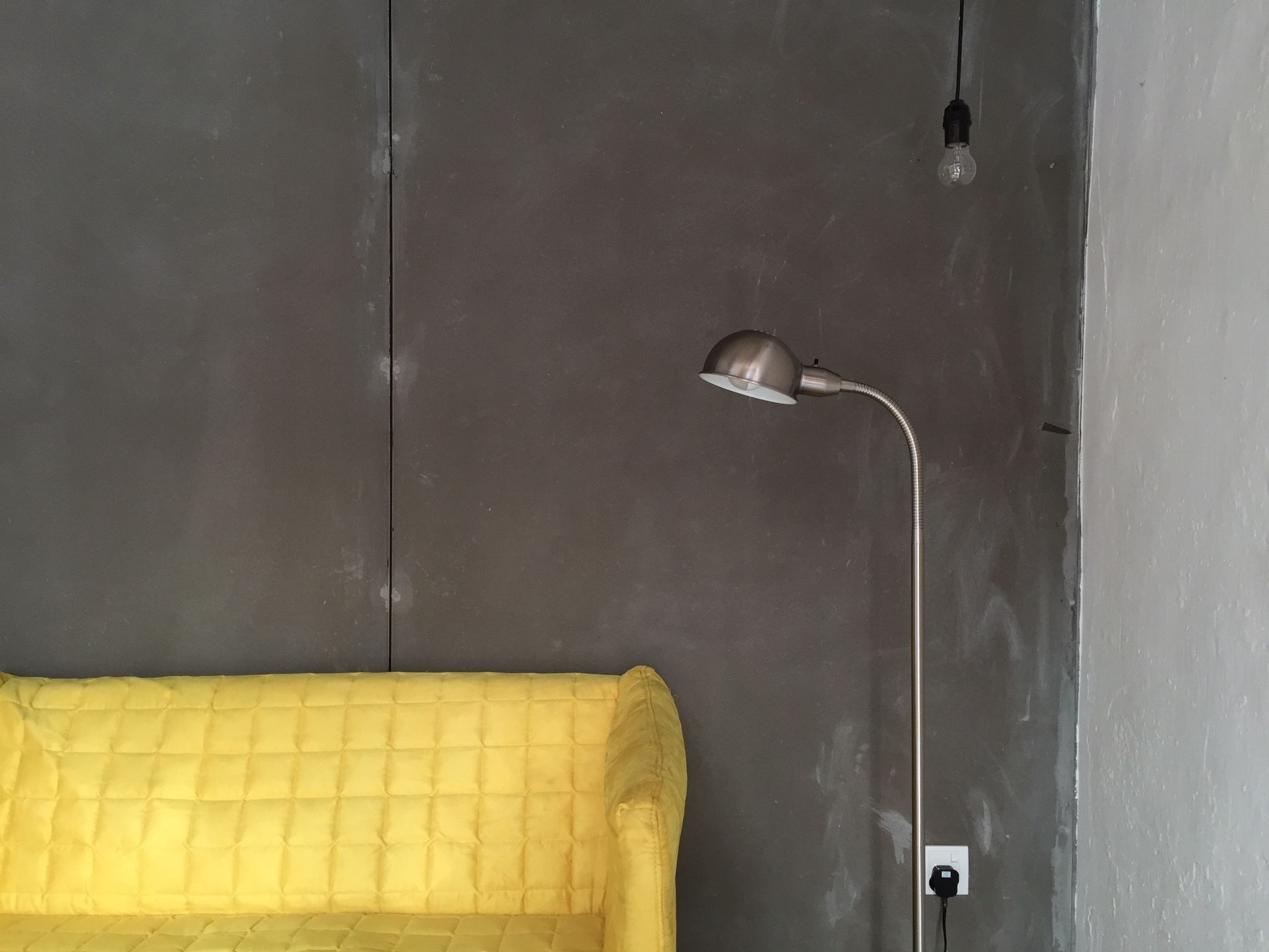 A yellow sofa against a grey wall with a single light bulb and a desk lamp.