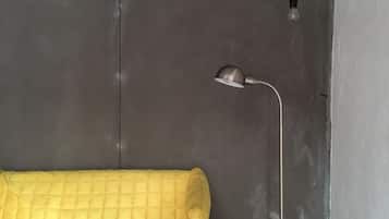 Ein gelbes Sofa vor einer grauen Wand, mit einer einzelnen Glühbirne und einer Schreibtischlampe.