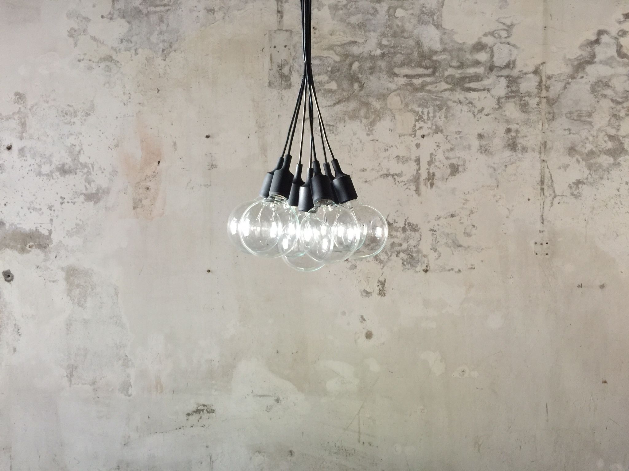 A pendant light fixture with multiple bulbs hanging from a single cord against a textured wall.