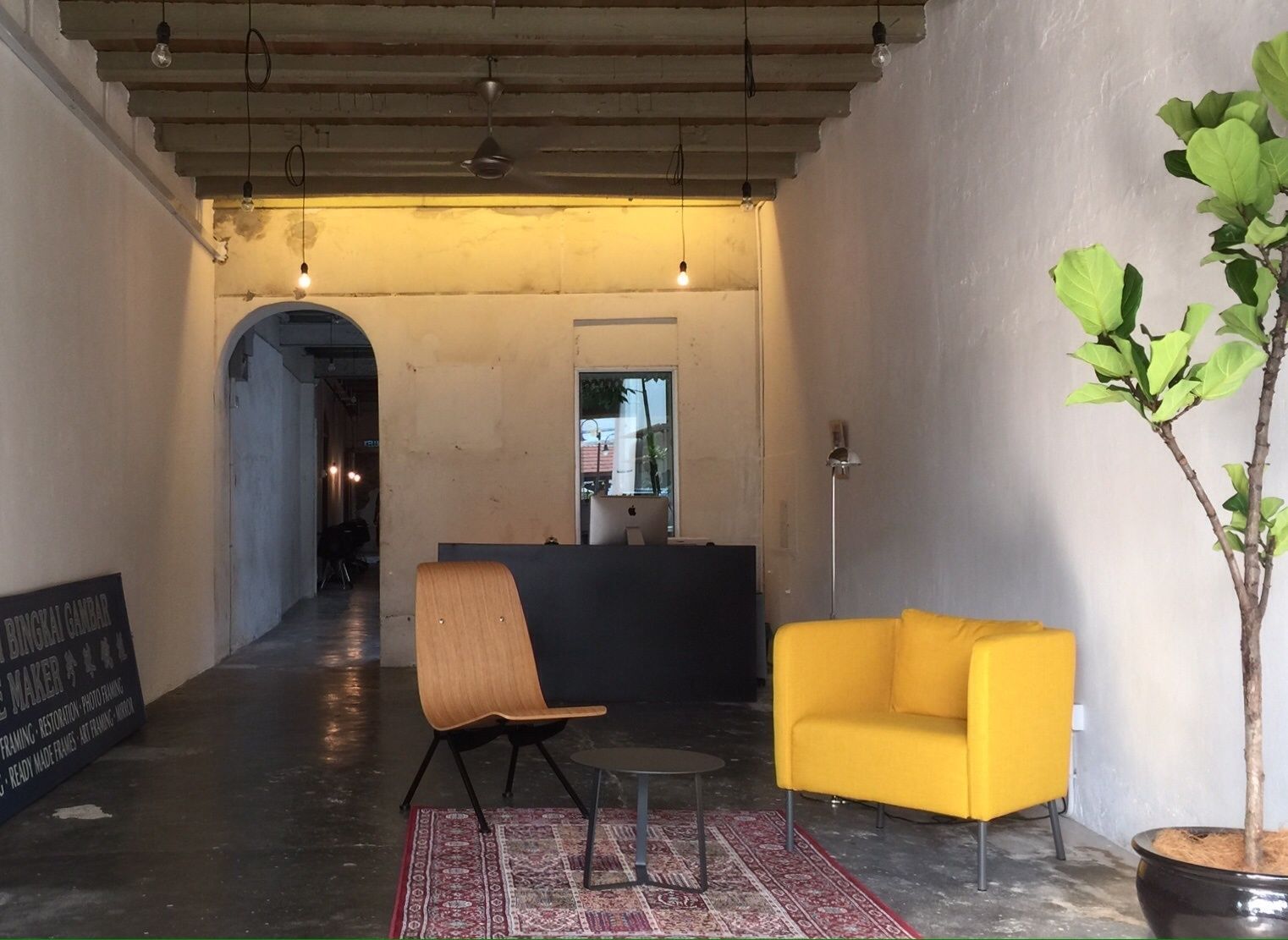 A reception area with a wooden chair, a yellow sofa, a potted plant, and a signboard.