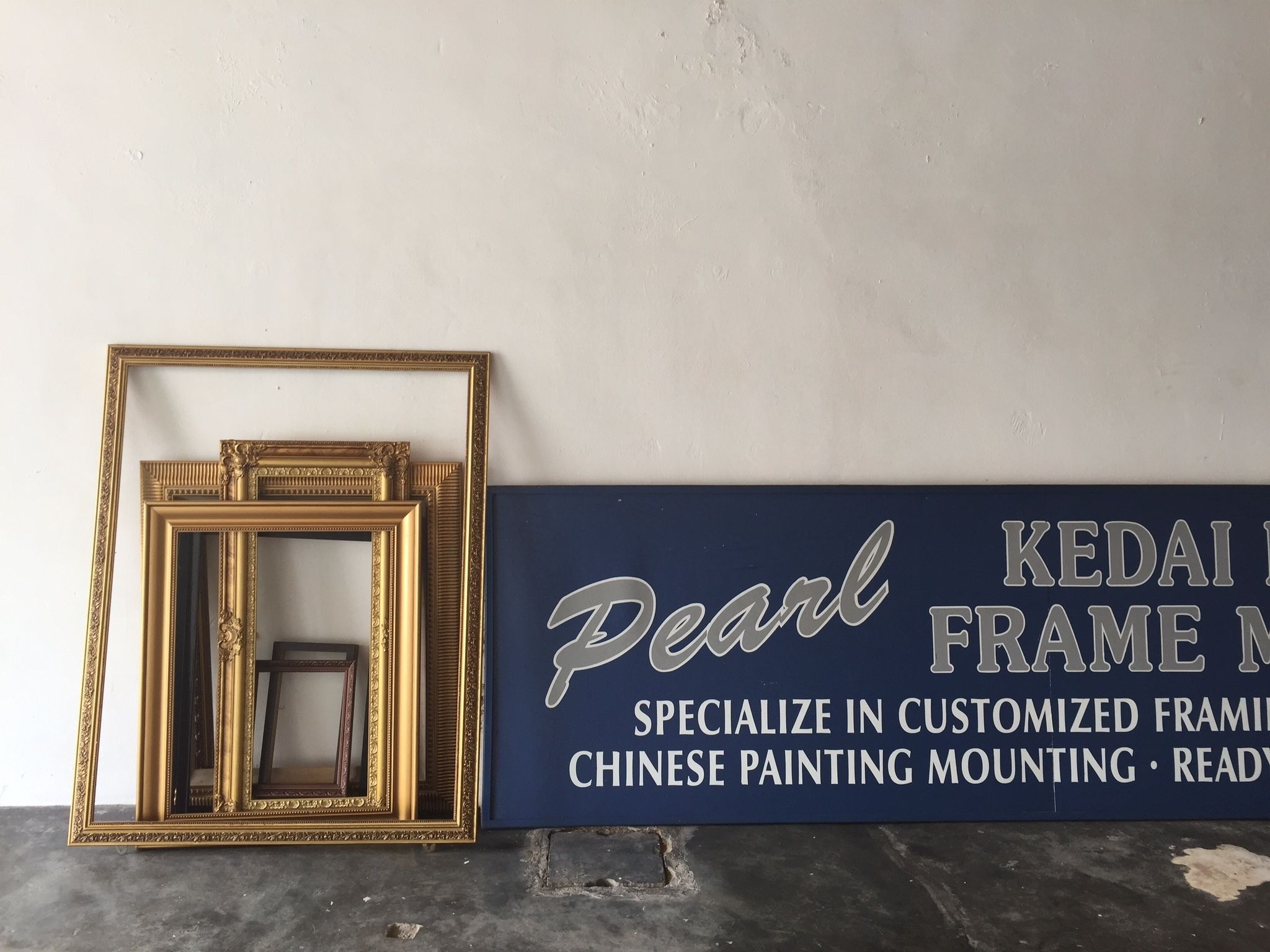 A signboard with the text "KEDAI FRAME" and "PEARL FRAME" alongside two ornate golden picture frames.