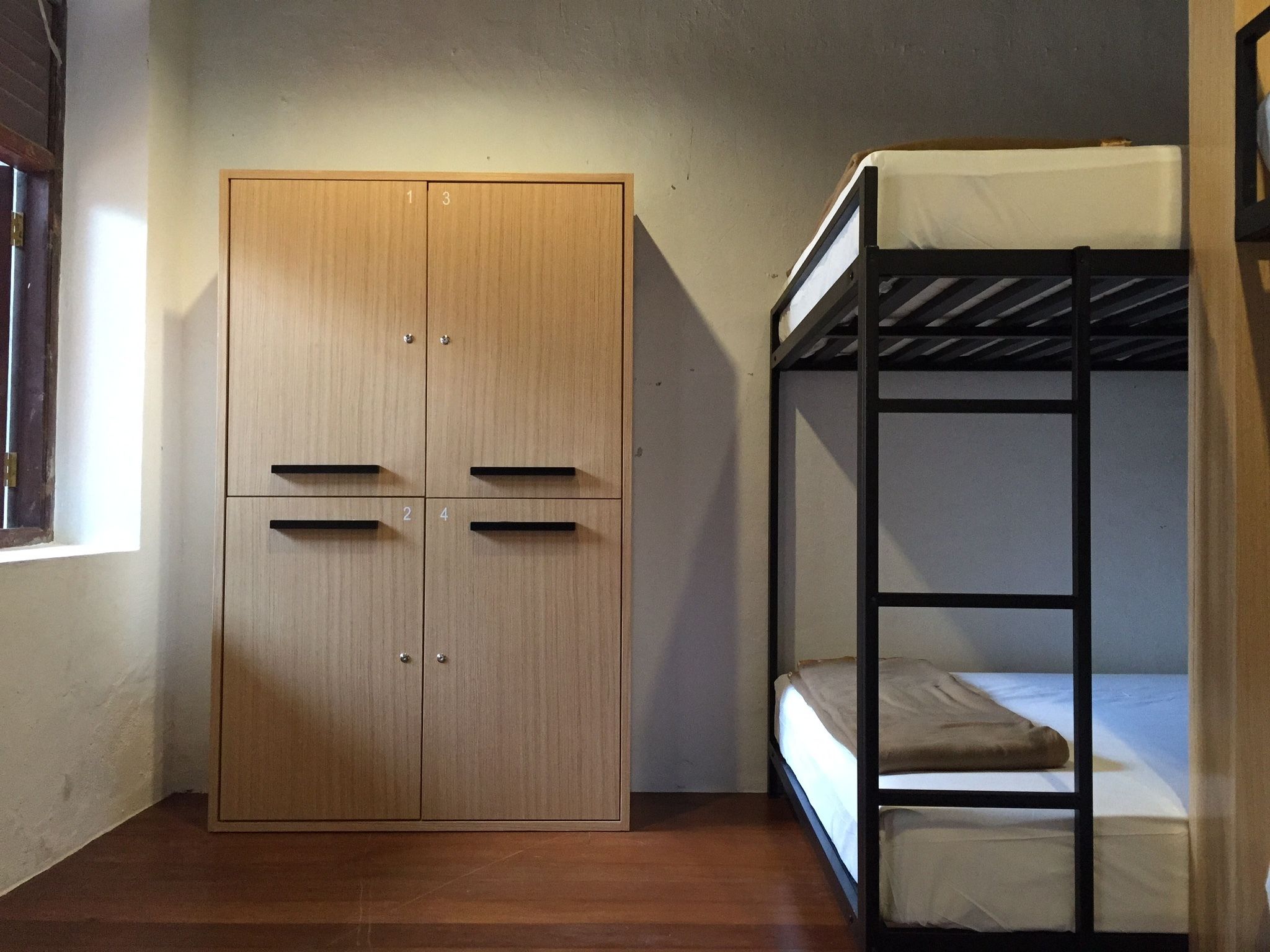 A room with a wooden wardrobe, a bunk bed, and a window.