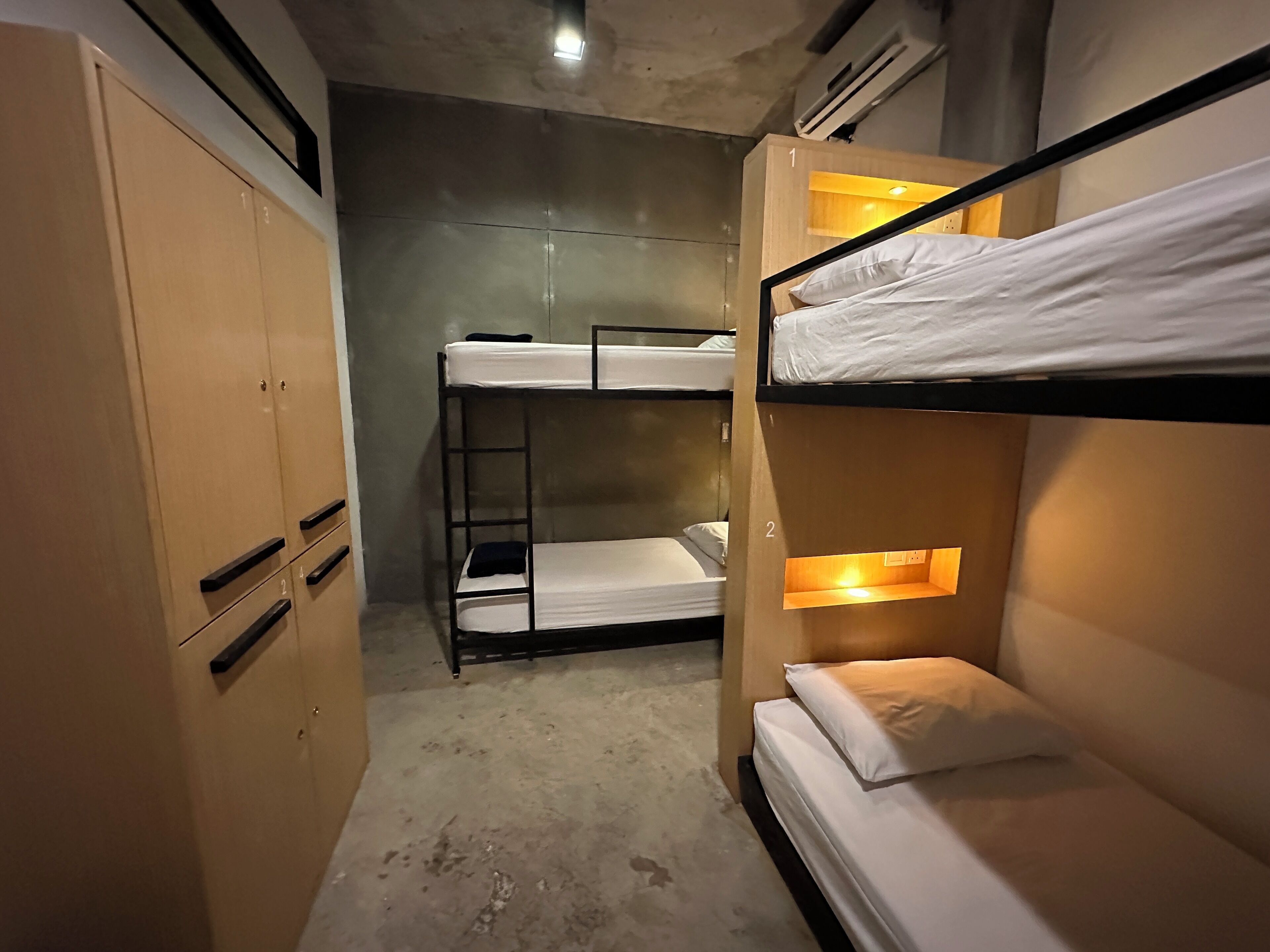 A bunk bed room with a wooden wardrobe and a concrete floor.
