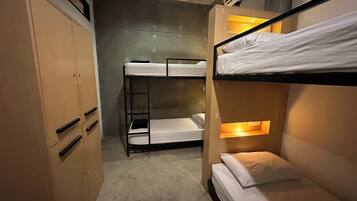 A bunk bed room with a wooden wardrobe and a concrete floor.