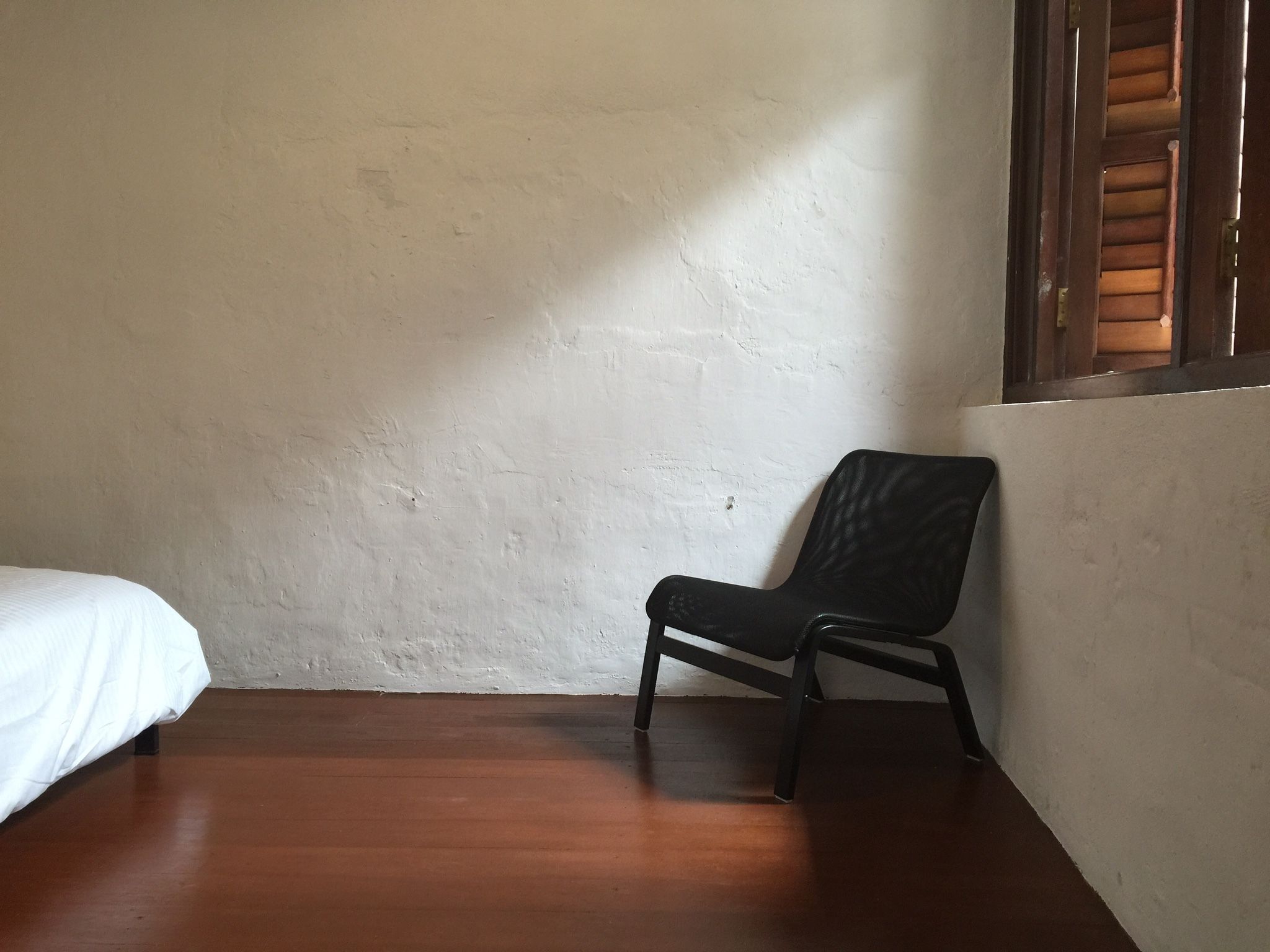 A room with a wooden floor, a white wall, and a black chair.