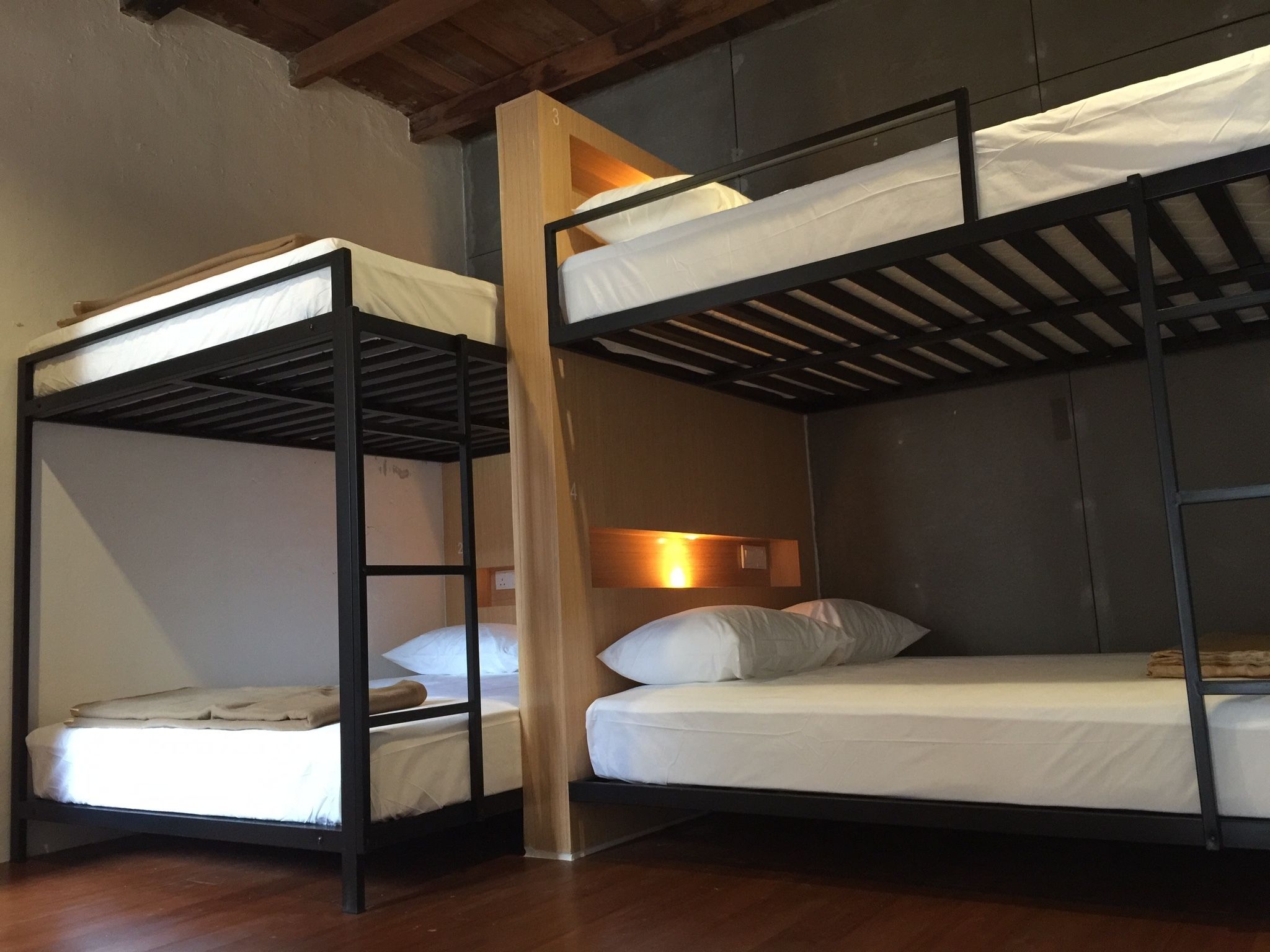 A room with two bunk beds, wooden beams on the ceiling, a wall-mounted light, and a wooden floor.