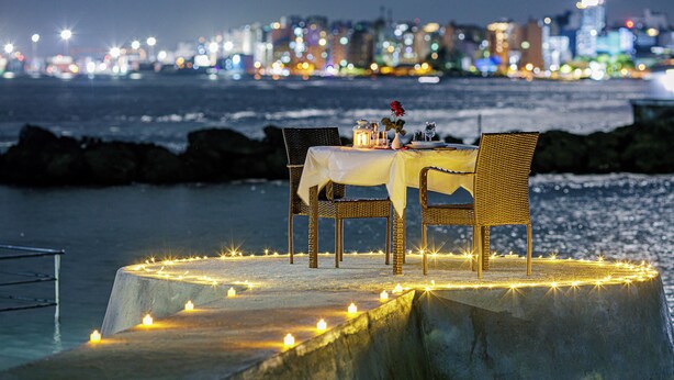 A table set up on a concrete platform with candles, overlooking a cityscape at night. - The Vinorva Maldives (Vilimalé)