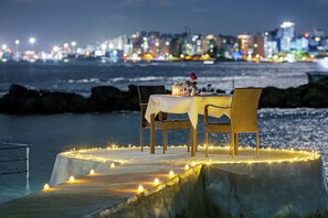 Une table dressée sur une plateforme en béton, décorée de bougies, d’où l’on peut admirer la vue sur la ville illuminée la nuit.