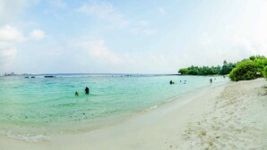 A beach with clear turquoise water, a sandy shore, and some greenery on the right. - The Vinorva Maldives (Vilimalé)