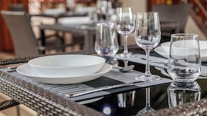 A dining table set with plates, glasses, and cutlery, with a wicker chair and a metal table frame. - The Vinorva Maldives (Vilimalé)