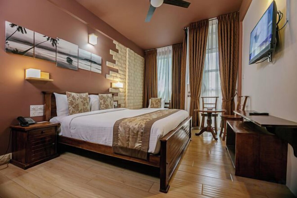 A hotel room with a large bed, bedside tables, a desk, and a TV on the wall.