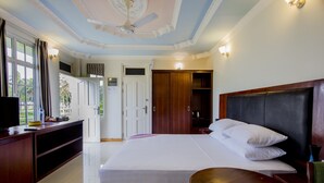 Una habitación de hotel con una cama grande, cabecera de madera, un televisor sobre un escritorio de madera y un ventilador de techo.