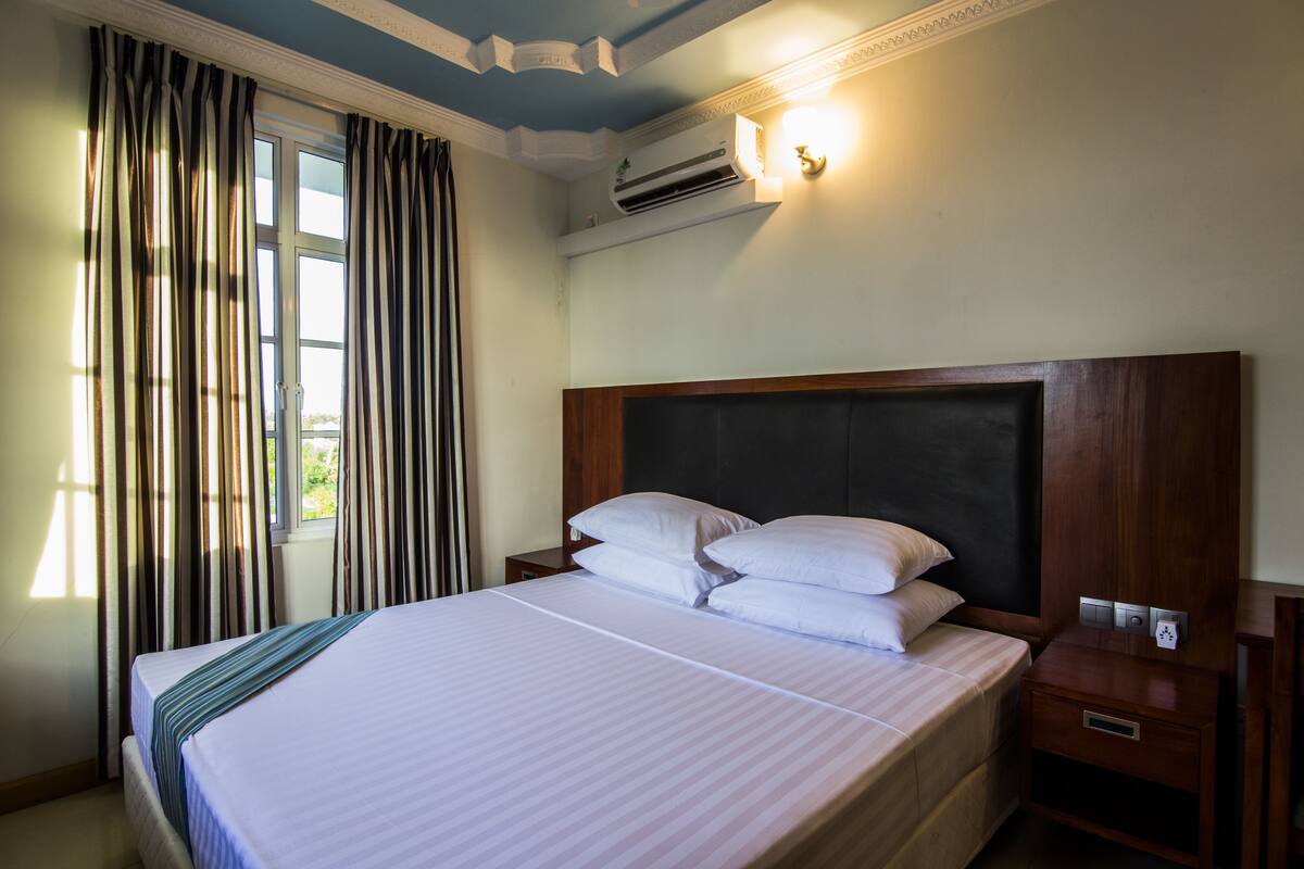 Une chambre d’hôtel avec un grand lit, une tête de lit en bois, une table de chevet et un climatiseur fixé au mur.