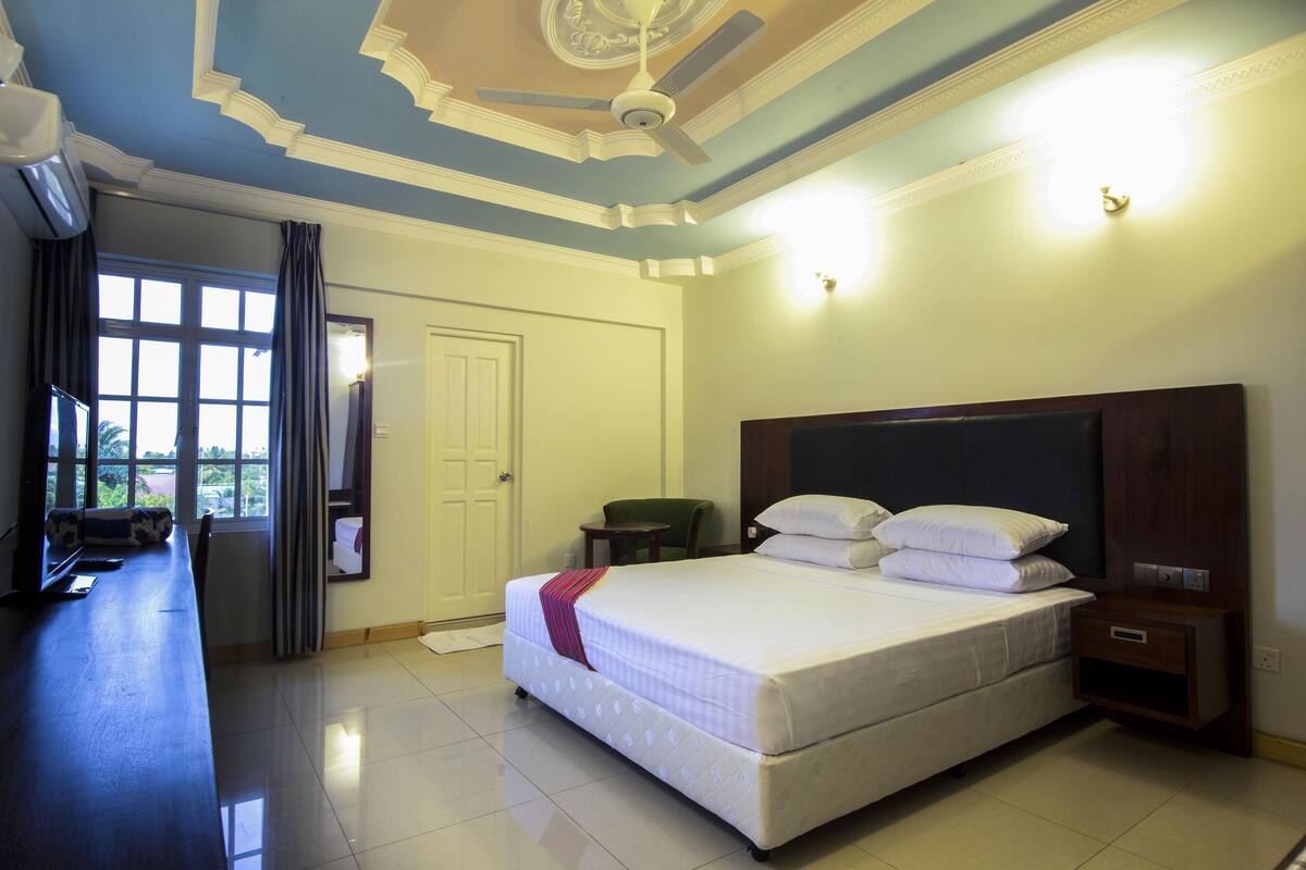 Une chambre d’hôtel avec un lit, un bureau, une chaise, une table de chevet et une fenêtre avec des rideaux.