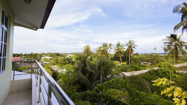 Un balcón con vistas a un paisaje tropical, con palmeras y una playa.