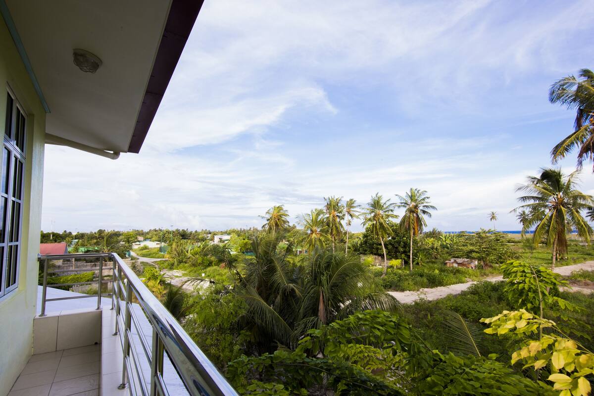 Un balcon offrant une vue sur un paysage tropical, avec des palmiers et une plage.