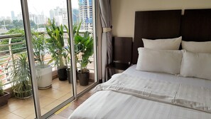 Une chambre à coucher avec un grand lit, une tête de lit sombre et une vue sur le paysage urbain, visible à travers une grande fenêtre.