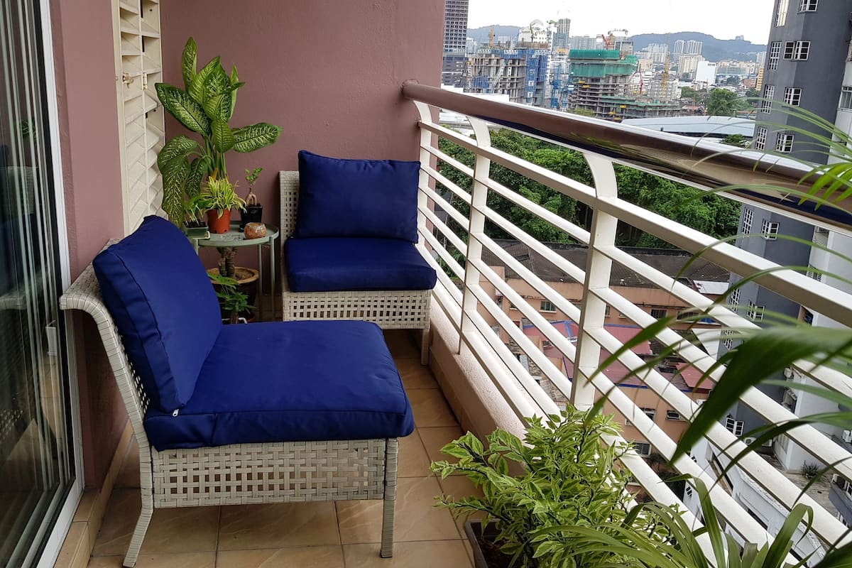 A balcony with two wicker chairs and a small table, surrounded by potted plants.