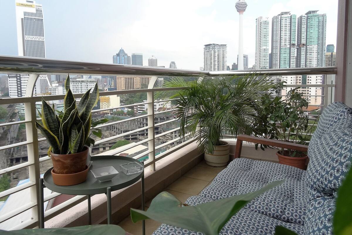 A balcony with a sofa, two potted plants, and a small table.