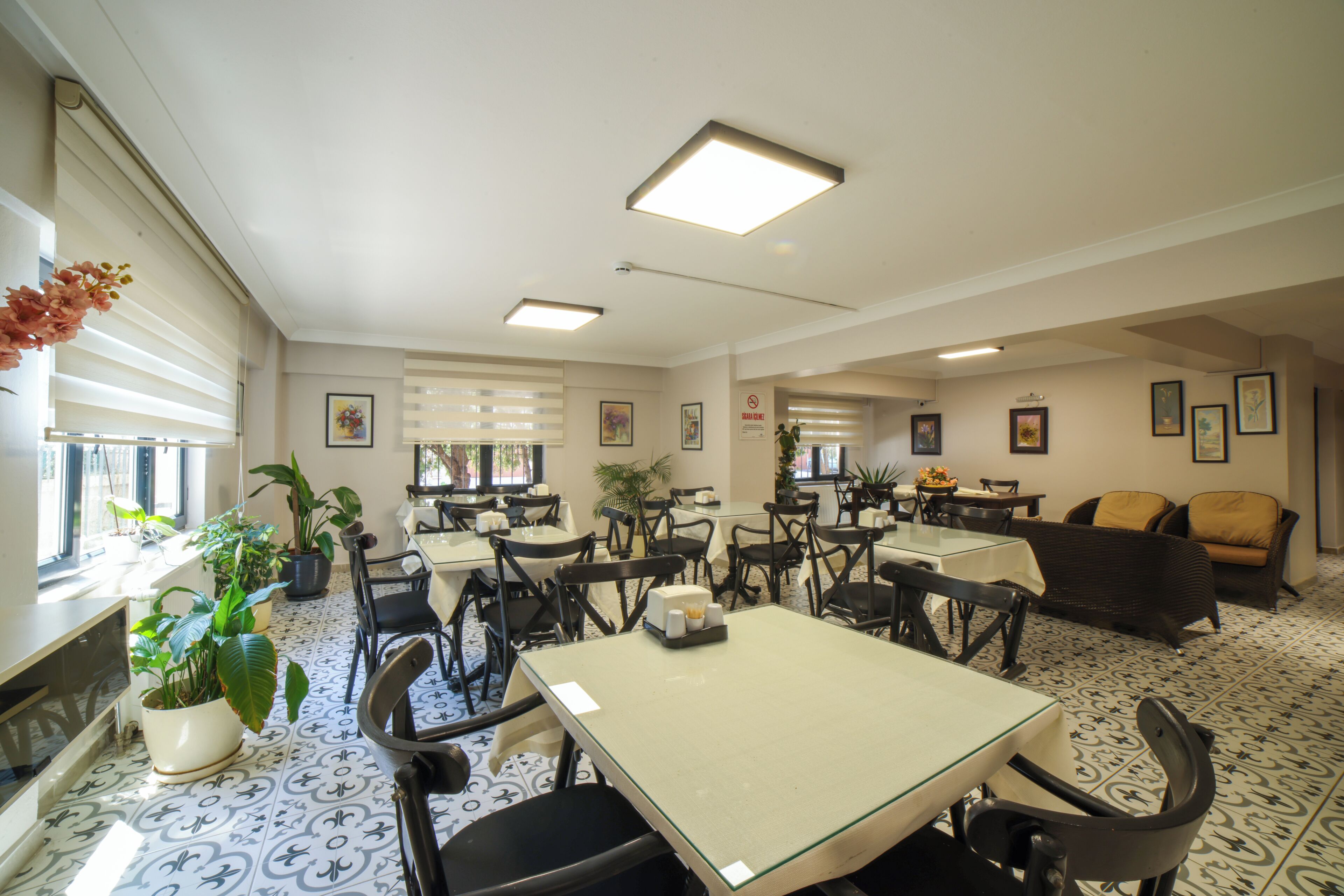 Un comedor de hotel con mesas, sillas, plantas en macetas y obras de arte en las paredes.
