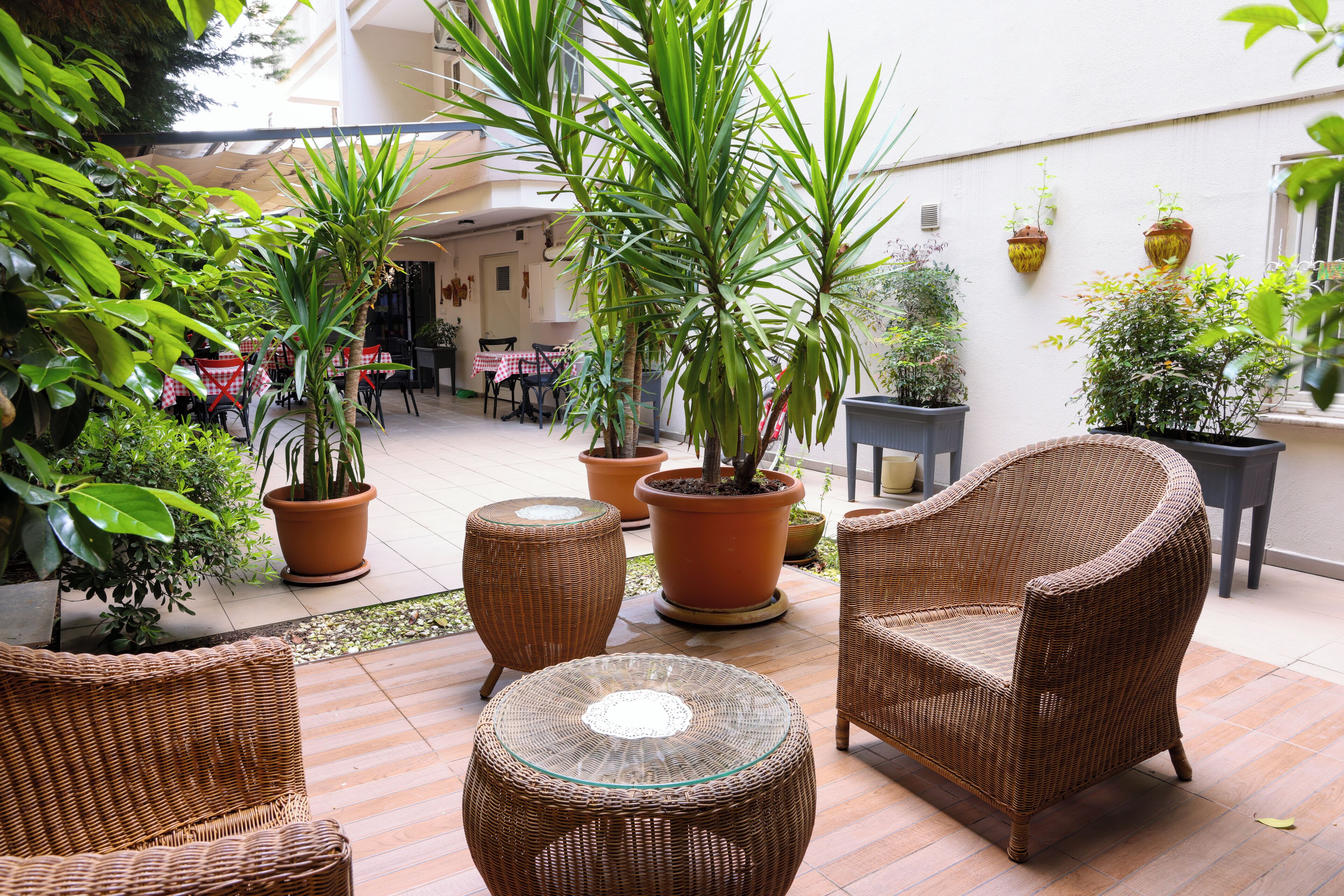A patio area with wicker furniture, potted plants, and a dining table with red and white checkered tablecloths.