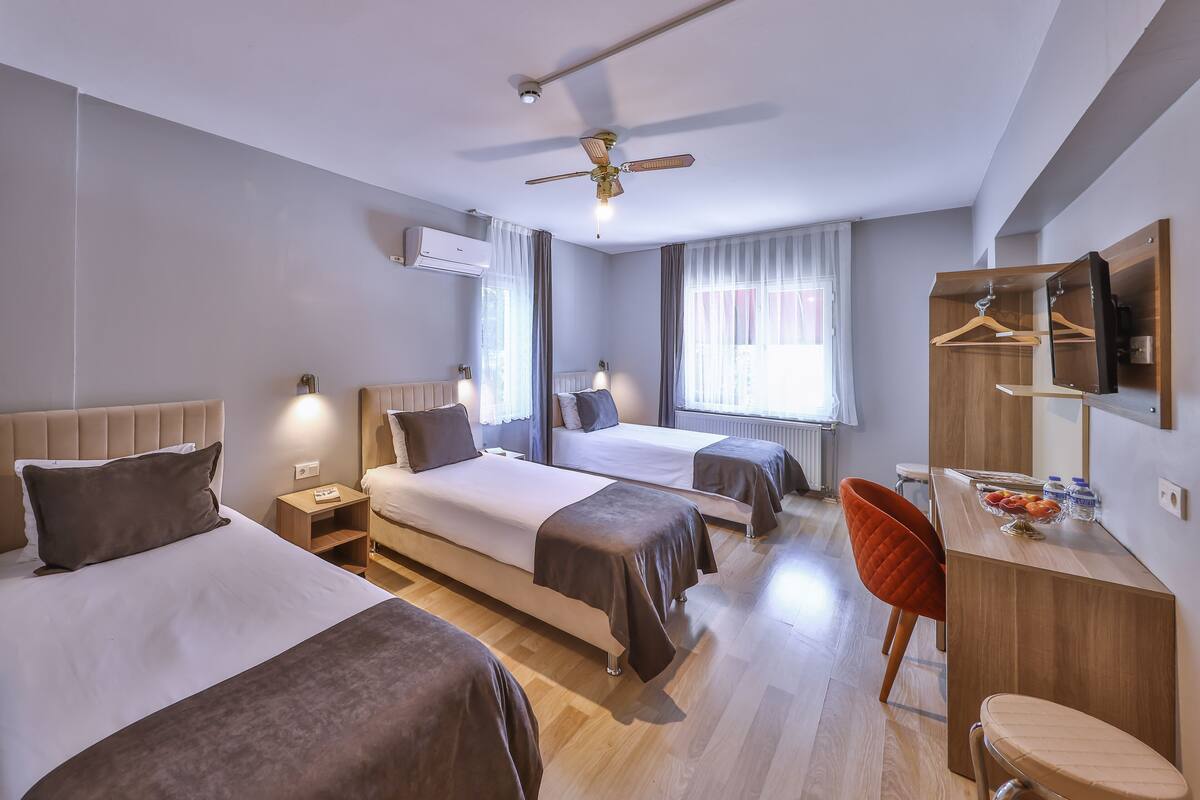 A hotel room with two beds, a desk, a chair, a ceiling fan, and a mirror.